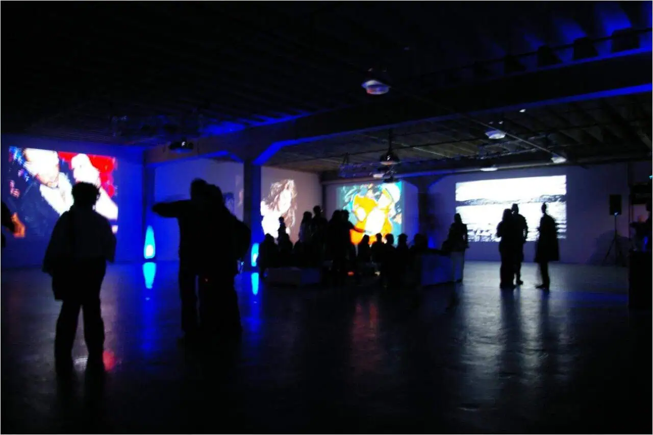 People are gathered in a dimly lit room with various projected artworks on the walls. The scene, featuring a blue hue, feels modern and immersive, like stepping through A Blue Door into another world. The event management has clearly put great thought into branding events uniquely and captivatingly.